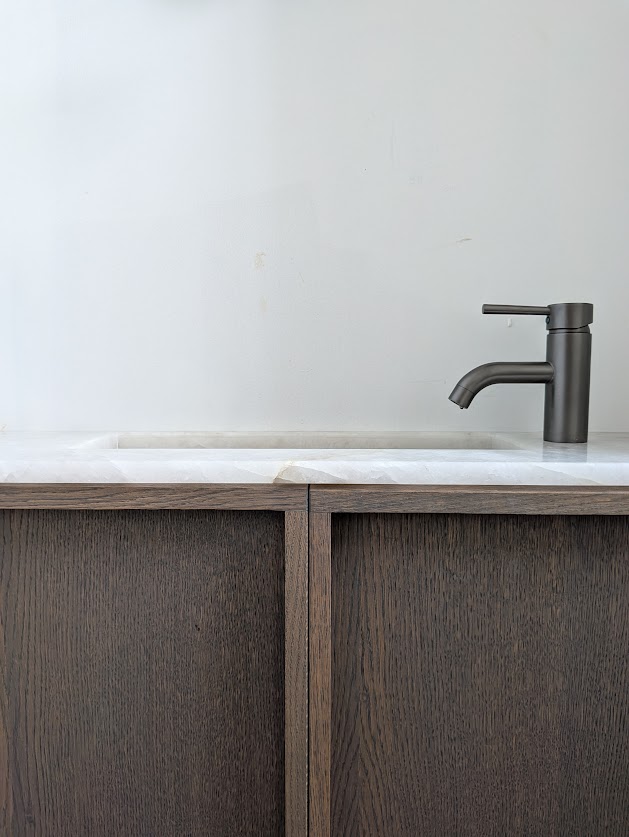 Meuble vasque en bois sombre sous un plan minéral et un robinet noir.